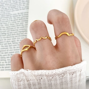 Detailed view of three minimalist wavy gold rings worn on fingers in a lifestyle setting
