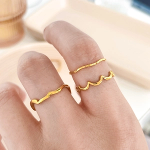 Detail of three minimalist gold-tone wave rings styled on fingers for a trendy look