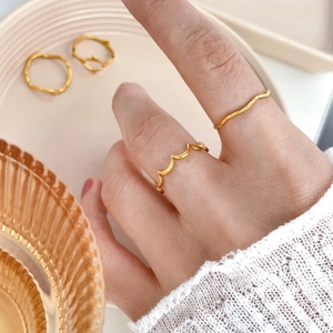 Close-up of wavy gold-plated rings in a minimalist style on fingers with warm textures