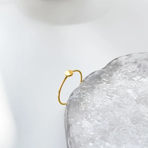 Dettaglio di un anello sottile in oro con disco piatto rotondo su un bordo di vetro