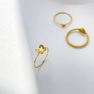 Dettaglio di un set di anelli dorati minimalisti con farfalla e cuore su sfondo bianco