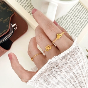 Set di tre anelli dorati con perle a cuore e quadrifoglio su sfondo di stile di vita chic