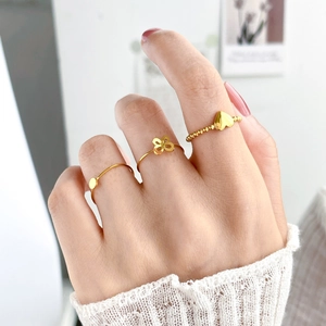 Dettaglio di tre anelli placcati oro con motivi a cuore, quadrifoglio e disco su modella