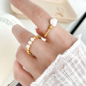 Detailed view of two 18K gold-plated steel rings with freshwater pearls on hand