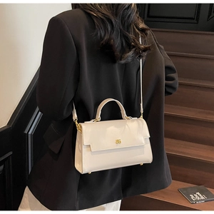 Detail of beige crossbody bag with gold buckle on a model in a minimalist outdoor setting