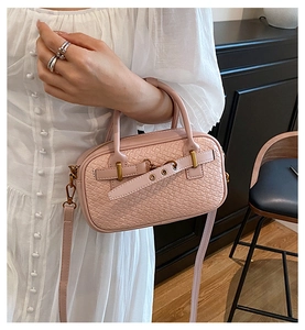 Détail du sac à main tissé rose clair avec fermoir doré porté sur une robe blanche