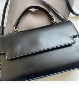 Detail of black leather flap handbag with gold metal logo and detachable shoulder strap