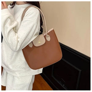 Detail of a brown and beige leather tote bag with gold bow logo worn by a model