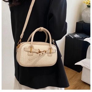 Vue latérale d'un sac Boston tressé crème avec détails dorés porté en bandoulière chic