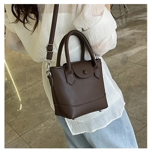 Detail of dark brown leather tote bag showing handle texture and adjustable strap in use