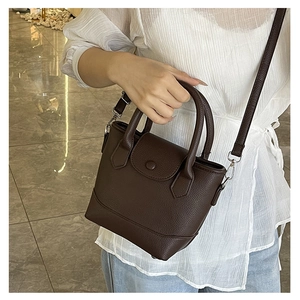 Detail of a dark brown pebble leather bucket bag with dual ring handles and snap flap