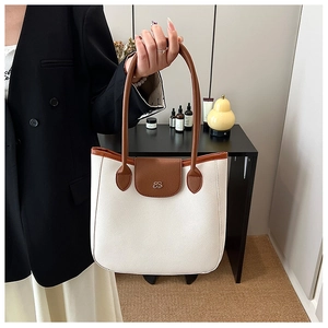 Detail of a chic cream and brown leather tote bag with gold logo on a modern tabletop