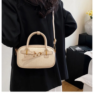Détail du mini sac Boston crème au motif tressé porté par un modèle avec boucles dorées