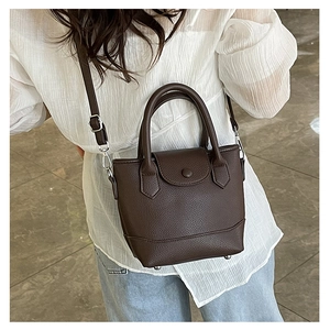 Detail of dark brown lychee leather bucket bag with top handles and adjustable strap
