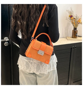 Detail showing orange woven texture box bag with silver metal buckle in a lifestyle setting