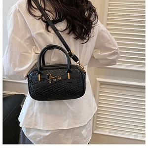 Détail d'un sac bowling noir texturé avec boucle dorée porté par un mannequin en chemise