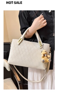 Detail of cream embossed leather tote with chain texture and teddy bear charm accessory