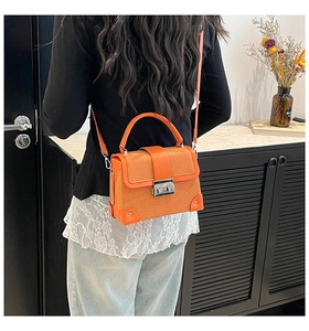 Detail of bright orange faux leather crossbody bag with snakeskin texture flap and silver lock