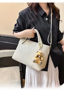 Detail of beige tote bag featuring embossed chain pattern and cute bear accessory