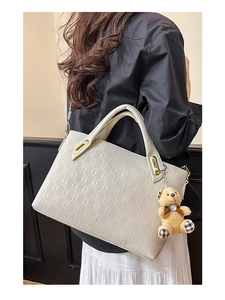 Detail view of cream handbag with chain texture and brown teddy bear charm on model