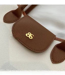 Detail of white litchi pattern leather stitched with brown leather and a gold logo