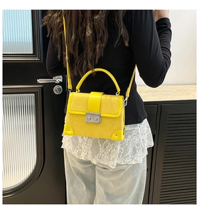Detail view of mustard yellow faux snakeskin box bag with metal lock and rivets