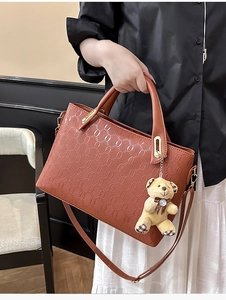 Close-up of caramel brown handbag with ring embossed texture and plush bear charm