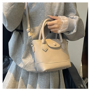 Close-up of beige lychee grain leather bucket bag with top handles and adjustable strap