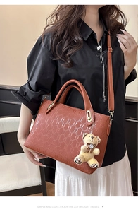 Macro detail of brown embossed PU leather handbag featuring a cute plush bear charm