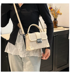 Close-up of cream woven texture handbag with metallic lock and crossbody strap