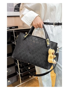 Close-up of black embossed tote bag with gold hardware and a cute teddy bear charm