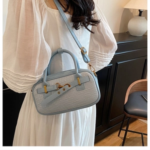 Sac à main en similicuir bleu clair avec motif crocodile porté par un mannequin chez soi