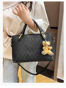 Detail of black embossed handbag featuring gold hardware and a cute teddy bear charm