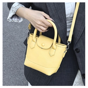 Detail of yellow pebbled leather bucket bag with silver hardware on a striped blazer