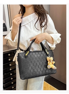 Detailed view of black textured tote bag with chain pattern and cute bear charm