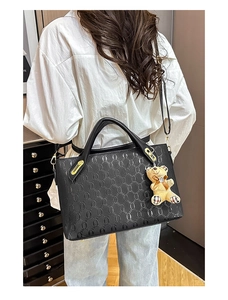 Detail of black embossed tote bag featuring elegant geometric texture and bear pendant