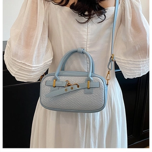 Détail du sac à main bleu clair avec texture tissée et garniture dorée sur mannequin