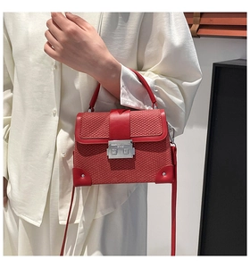 Macro view of red snakeskin textured box bag with silver metal push-lock and top handle