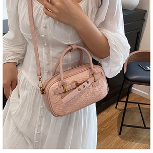 Détail d'un sac à main rose clair à texture tressée avec garnitures dorées sur robe