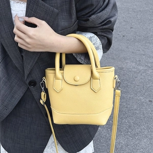 Bright yellow minimalist bucket bag in pebbled leather with top handle and crossbody strap
