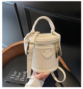 Detail of off-white woven bucket bag featuring silk scarf handle and gold hardware accents
