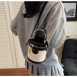 Detail of a woven bucket bag featuring contrasting colors and silk scarf handle decor