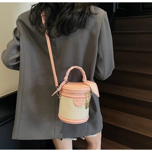 Model wearing a pink and beige woven bucket bag with scarf handle on a wooden staircase