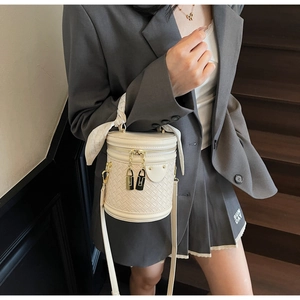 Detail of white woven bucket bag with gold hardware and decorative silk scarf handle