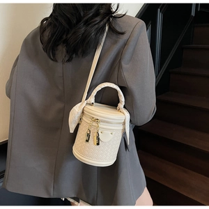 Detail of cream woven bucket bag with gold zipper and decorative silk scarf handle