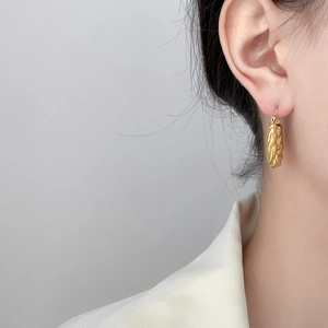 Detail of twisted gold rope earrings in stainless steel on female model ear