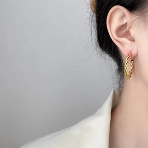 Close-up of golden twisted rope hoop earrings with textured finish on model