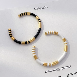 Detail of gold-plated twisted bangles with black and white enamel on a white book