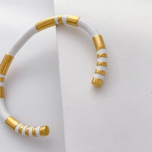 Macro detail of enamel bangle with gold metal accents on textured white paper