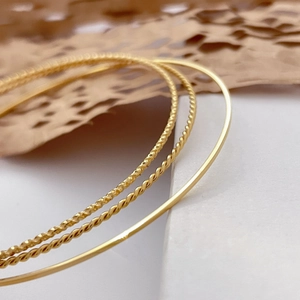 Detailed macro view of three textured gold-plated bangles on a white marble surface